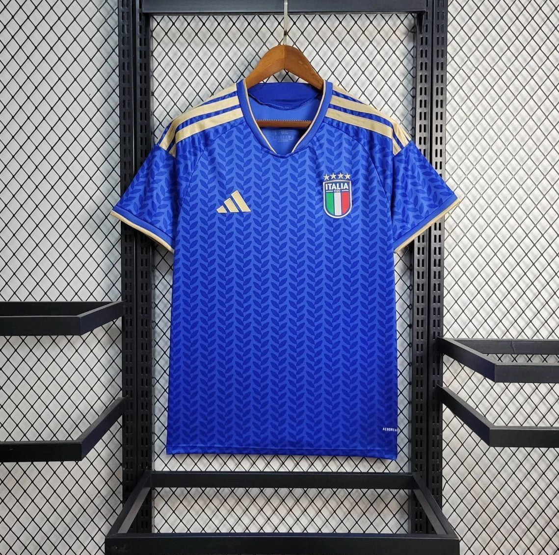 Blue Italy Home  jersey with Italian flag emblem on a hanger against a grid background