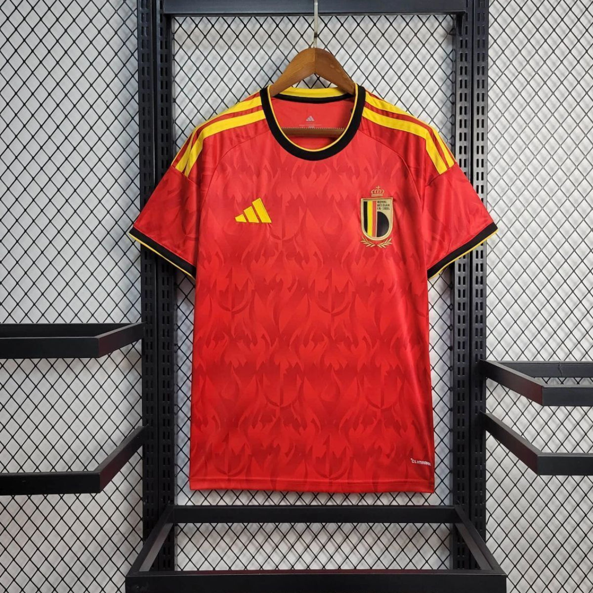 Red belgium jersey with yellow accents on a hanger against a black metal rack.